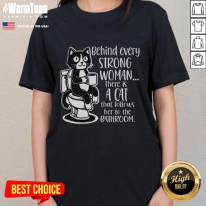 Funny women's tee featuring the phrase 'Behind Every Strong Woman, There's A Cat That Follows Her To The Bathroom.'